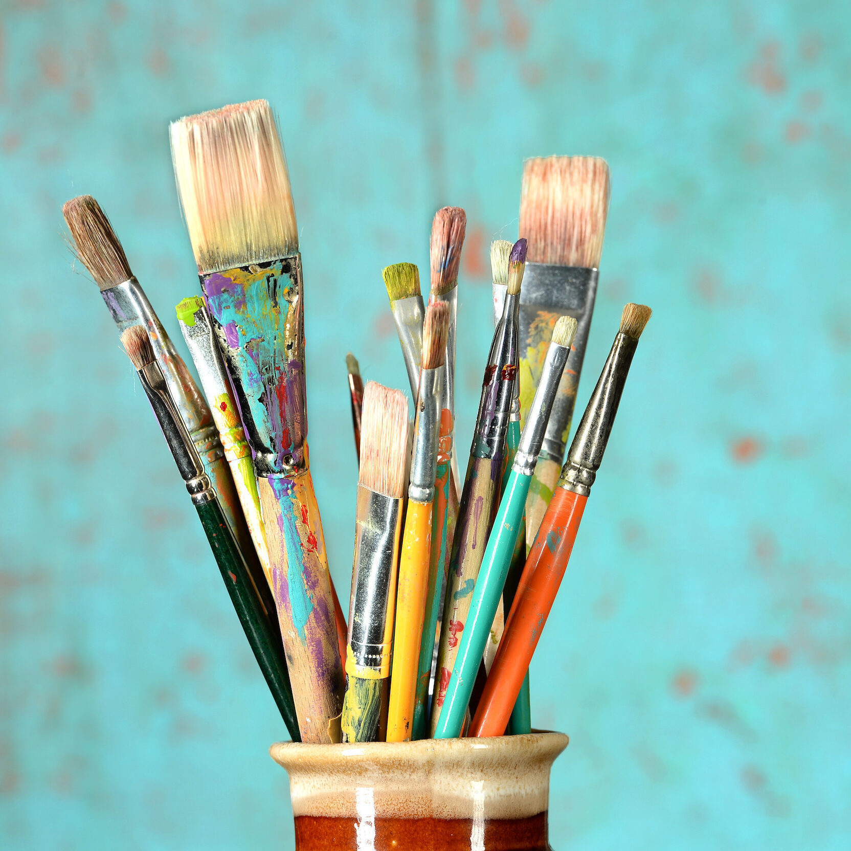 Artist paintbrushes in a jar over colorful background